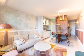 Ein modernes Wohnzimmer mit einer Couch, einem runden Tisch und einer Küchenzeile mit Schränken und einem Esstisch.