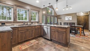 A kitchen with wooden cabinets, a dishwasher, and a dining area with a table and chairs. - 2 Bedroom Cabin with Fireplace (West Glacier)