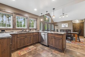 A kitchen with wooden cabinets, a dishwasher, and a dining area with a table and chairs. - 2 Bedroom Cabin with Fireplace (West Glacier)