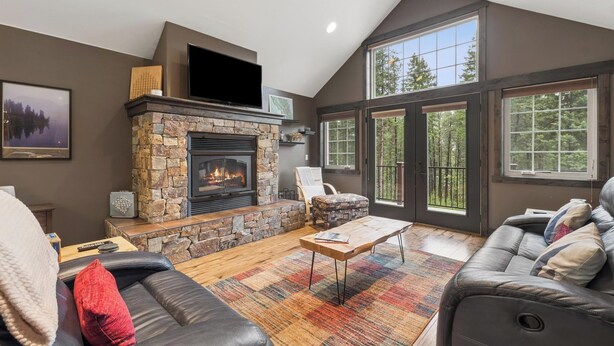 A living room with a stone fireplace, leather sofa, and large windows. - 2 Bedroom Cabin with Fireplace (West Glacier)