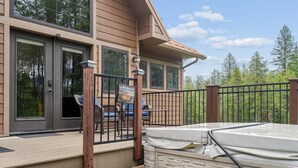 A wooden deck with outdoor furniture, a hot tub, and a view of trees. - 2 Bedroom Cabin with Fireplace (West Glacier)