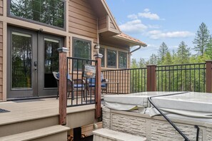 A wooden deck with outdoor furniture, a hot tub, and a view of trees. - 2 Bedroom Cabin with Fireplace (West Glacier)