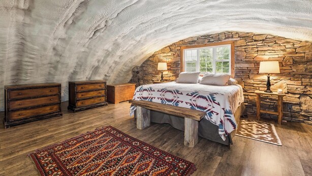 Une chambre avec un mur en pierre, des meubles en bois et un tapis à motifs.