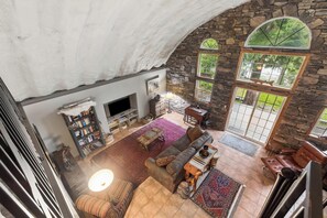 A spacious living area with a stone wall, a large window, a fireplace, and a television. - Two Bedroom Quonset Hut on Spoon Lake (Columbia Falls)