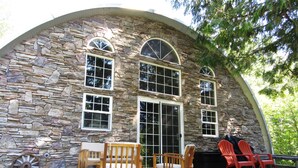 Un bâtiment en pierre doté d’un toit incurvé, de grandes fenêtres, d’une terrasse en bois et d’un espace salon extérieur.