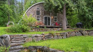 Une maison en pierre avec un toit incurvé, entourée d’un mur de pierre et d’une zone herbeuse.