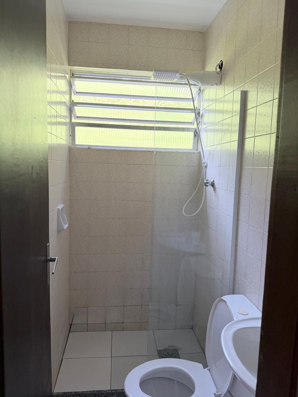 Een kleine badkamer met tegels, een toilet, een douchegedeelte en een raam.