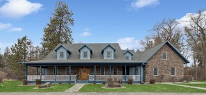 A two-story house with a stone facade, a front porch with white railings, and a gabled roof. - Five Bedroom 4 Bath Private Ranch House (Columbia Falls)