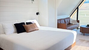 A bedroom with a large bed, a sofa, and a view of the outdoors. - Cozy Luxe Cabin w/Hot Tub, Fire Pit & Stunning Views (Bozeman)