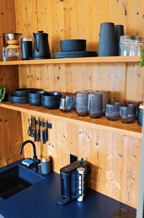A kitchen with wooden shelves holding various kitchenware, a sink with a faucet, and a countertop with a coffee machine.
