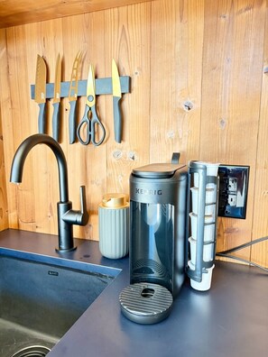 A kitchen with a coffee maker, a sink, and utensils hanging on the wall.