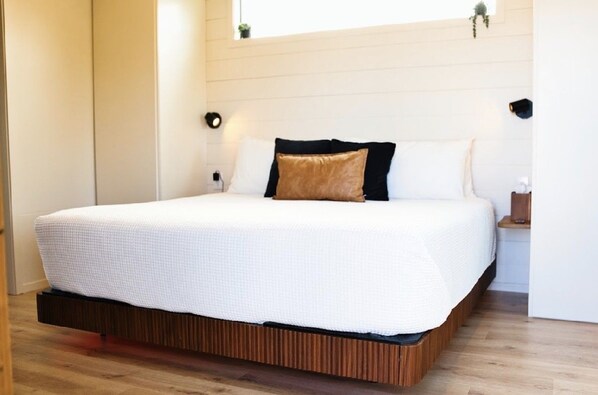 A neatly made bed with a white bedspread, a brown pillow, and two black pillows.