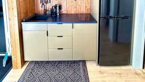 A compact kitchen with wooden shelves, a stainless steel refrigerator, and a black countertop. - Cozy Luxe Cabin w/Hot Tub, Fire Pit & Stunning Views (Bozeman)