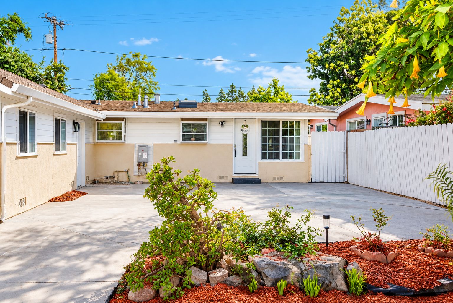 A residential property with a covered patio, a small garden with rocks and plants, and a white fence.