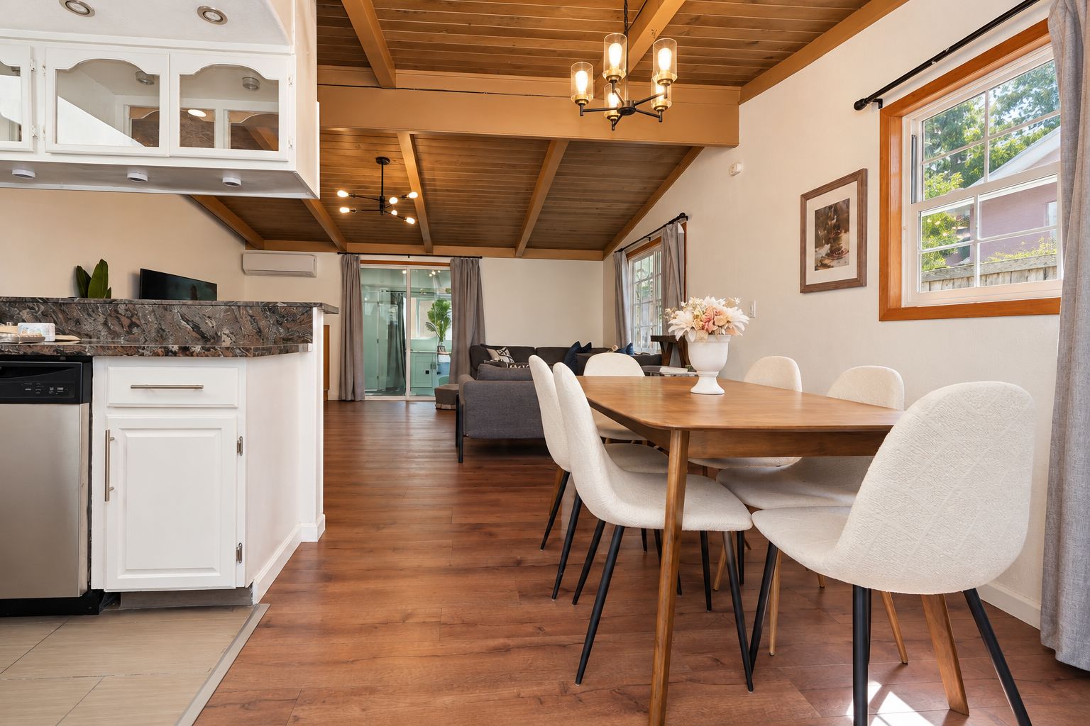 A modern kitchen with white cabinets, a marble countertop, and a dining area with a wooden table and white chairs.