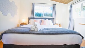 A neatly made bed with a grey blanket, white pillows, and rolled towels. There is a window with curtains, a wooden ceiling, and a wall-mounted light fixture. - Central 3BR 2BA Near Santana Row & Valley Fair (San Jose)