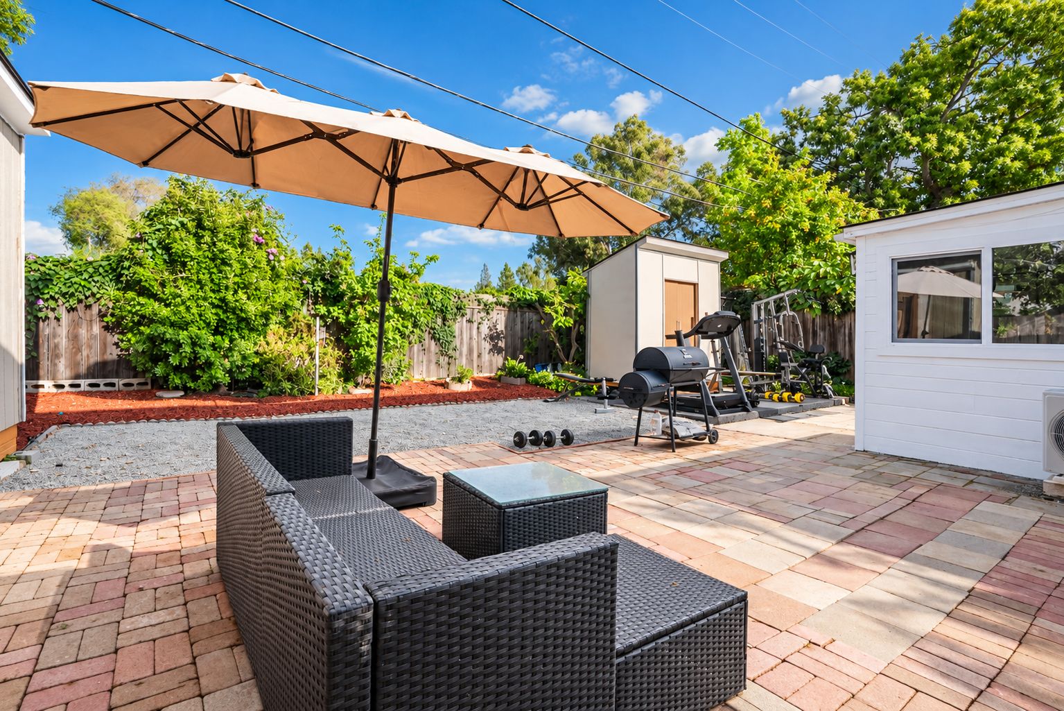 Een terras buiten met rieten meubels, een barbecue en een kleine schuur.