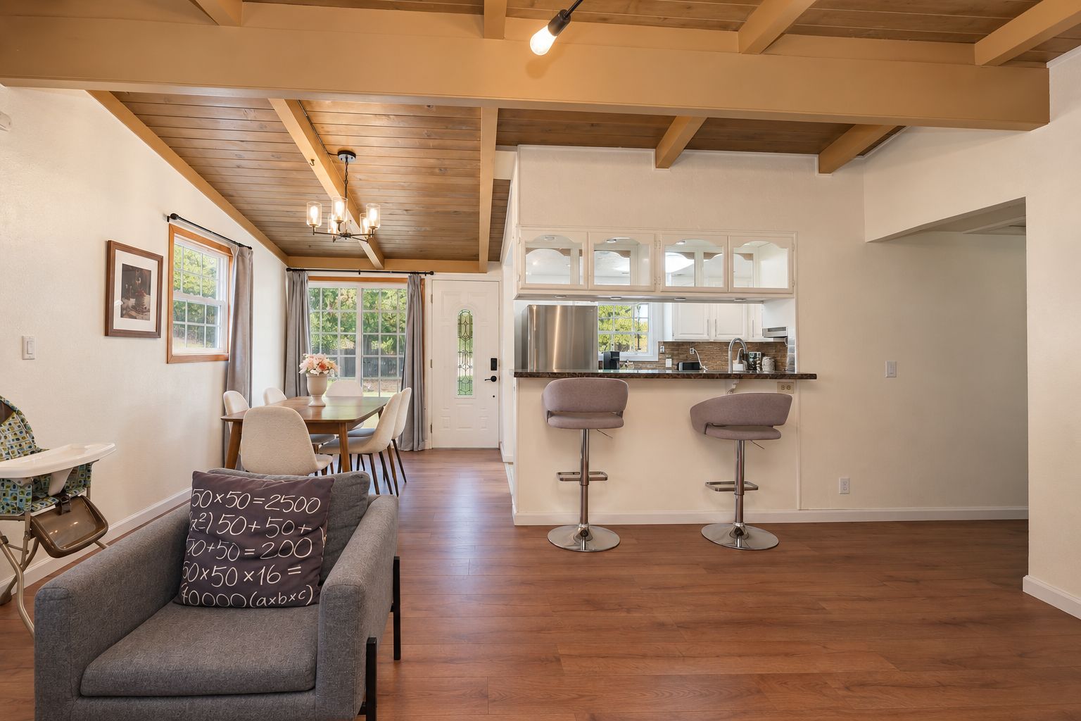 A modern kitchen with stainless steel appliances, a dining area with a table and chairs, and a living room with a sofa and a baby high chair.