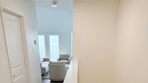 A narrow hallway with a wooden staircase and a white bench.