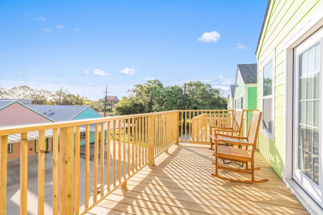 Eine Holzdar Terrasse mit Geländer, zwei Holzstühle und Blick auf ein grünes Gebäude.
