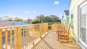 A wooden deck with a railing, two wooden chairs, and a view of a green building.