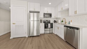 A modern kitchen with white cabinetry, stainless steel appliances, and a wooden floor.