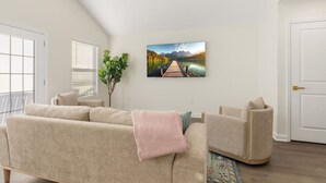 Un soggiorno con un divano color beige, una poltrona, una pianta in vaso e un quadro raffigurante un lago e delle montagne.