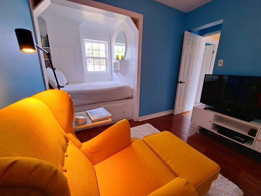A bedroom with a bed, a TV, and a bright orange chair.
