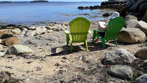 Two green chairs on a rocky beach with a view of the water and distant land.