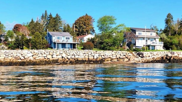A waterfront property with a stone wall, houses in the background, and calm water.