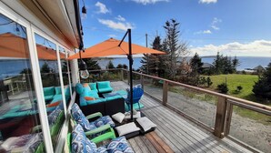 A deck with outdoor seating, a view of the sea, and a wooden railing.