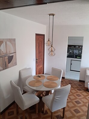 A dining area with a round table, four chairs, a wooden door, and hanging pendant lights. - Apartamento com 2 quartos, a 15 minutos da praia Barra da Tijuca,  RJ, Brasil (Rio de Janeiro)