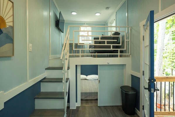 A room with a bunk bed, a staircase, a door, and a trash bin. - Harbor Blue (Anderson)