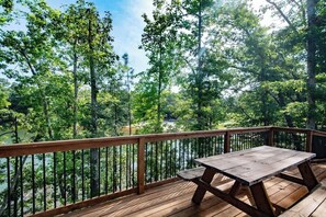 A wooden deck with a picnic table overlooking a river surrounded by trees. - Harbor Blue (Anderson)