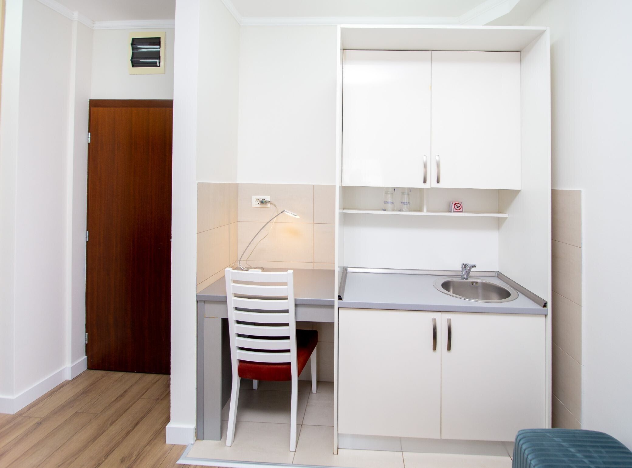 A compact kitchenette with a sink, cabinets, and a chair.