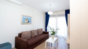 Uma sala de estar com um sofá marrom, uma mesa branca, um quadro e uma janela com cortinas.