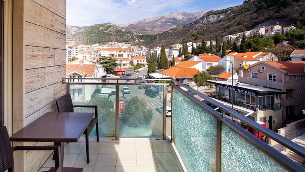 Uma varanda com mesa e cadeiras, com vista para um horizonte urbano com edifícios e uma montanha ao fundo.