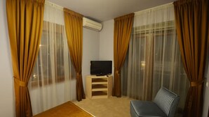 Une chambre d’hôtel avec un lit, un téléviseur posé sur un meuble, un canapé et des rideaux.
