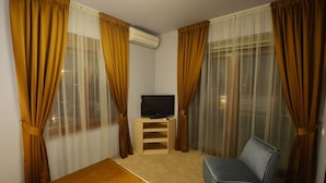 Una habitació d'hotel amb un llit, una televisió sobre un suport, un sofà i cortines.