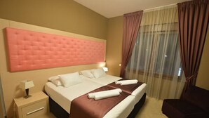 Una habitación de hotel con una cama grande, una mesita de noche, una silla y un ventanal con cortinas.