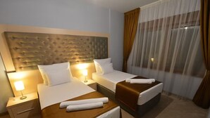 Habitación de hotel con dos camas, cabeceros, mesitas de noche, una lámpara y una ventana con cortinas.