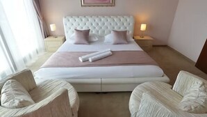 Een hotelkamer met een groot bed, twee nachtkastjes, twee fauteuils en een lijst met een afbeelding aan de muur.