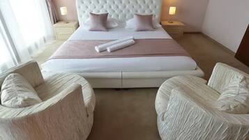 Una camera d'albergo con un letto grande, due comodini, due poltrone imbottite e un quadro incorniciato appeso al muro.