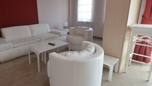 Ein stilvolles Wohnzimmer mit einem weißen Sofa, einem runden weißen Hocker, einem kleinen weißen Tisch und einem weißen Beistelltisch.