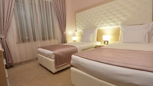 Ein Hotelzimmer mit zwei Betten, einem großen Fenster mit durchsichtigen Vorhängen, einem gepolsterten Kopfteil, Nachttischlampen und einem Teppichboden.