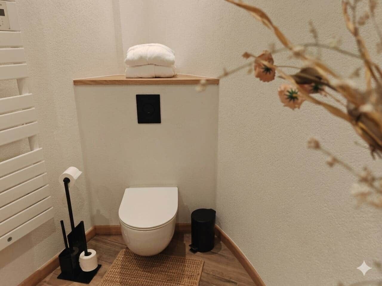 Une petite salle de bain comprenant des toilettes, une poubelle, un porte-rouleau de papier toilette et une serviette posée sur une étagère.