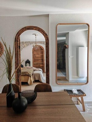 A bedroom with a wooden door, a large mirror, and a dining area with a table and chairs. - Les Chambres Côté Cour (Gex)