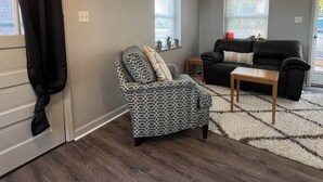 A living room with a patterned armchair, a black sofa, a wooden coffee table, and a rug. - Deaconess Gateway 3 miles, Quiet, Open, 1BDRM, Private Parking & More! (Evansville)