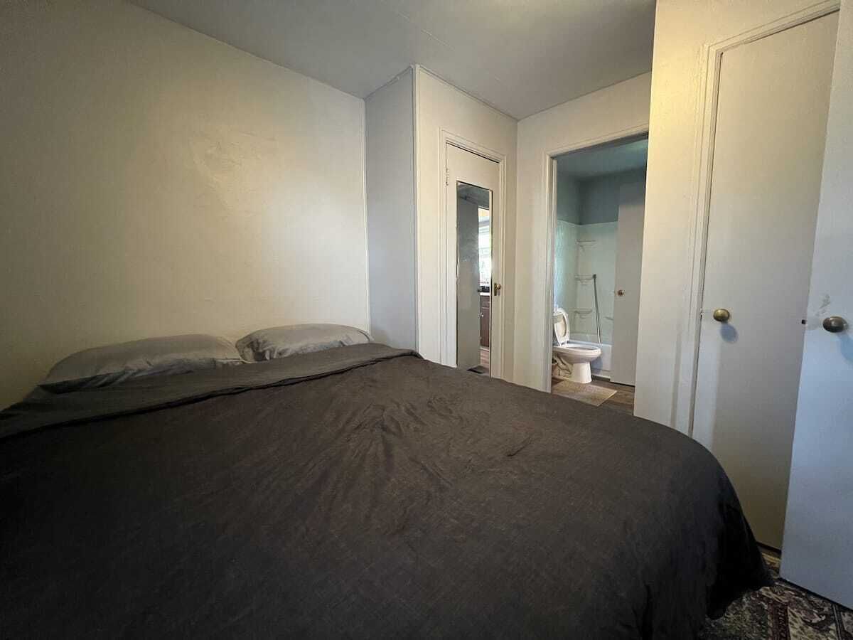 Un dormitorio con cama, una puerta que da a un baño y un inodoro visible.