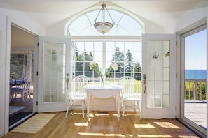 A room with a wooden floor, a white table with chairs, a glass door, and a view of the ocean. - Cliffside Oceanfront Bit of Heaven (Murray River)